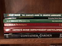 Photo of five books stacked horizontally showing their titles and spines on a wooden shelf.
