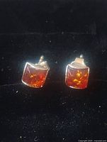 Front view of the sterling silver amber stud earrings on black background showing square amber stones and silver settings.