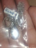 Close-up of locket pendant and chain held in hand inside clear plastic bag showing price tag $45.