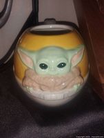 Front view showing detailed 3D Baby Yoda face and ears sculpted on the ceramic mug with yellow background