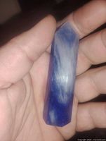 Photo showing blue quartz crystal point held in hand, displaying its polished surface and hexagonal shape with a sharp point.
