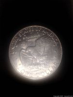Reverse side of a 1972 Eisenhower silver dollar coin showing an eagle landing on the moon carrying an olive branch with a Liberty Bell in the background.
