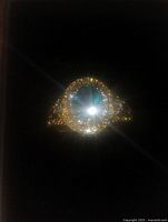 Front view of gold tone ring with large oval blue stone surrounded by clear crystals.