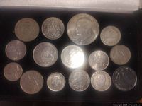 Top view of 16 various coins including a large US Eisenhower dollar and assorted quarters, pennies, and other coins.