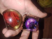 Hand-held view of the two paperweights showing the red swirled blown glass sphere and the resin crystal pyramid with purple galaxy and gold leaf detail.
