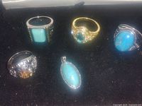 Photo showing four rings with turquoise and other stones plus one turquoise pendant on black velvet background.
