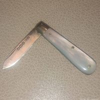 Folding knife open showing solid sterling silver blade with English hallmarks and mother of pearl handle, photographed on neutral surface.