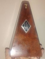 Front view of antique German metronome showing burl wood exterior and emblem.