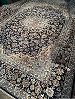 Full view of area rug laid flat, showing navy ground, central medallion and floral border