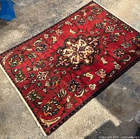 Top view showing the full red floral patterned rug with a central cream medallion on concrete floor.