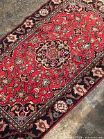 Corner view showing red field with central floral motif on concrete floor