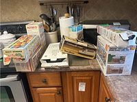 Photo showing multiple kitchen appliances and utensils on a kitchen counter including boxed items and utensil holders