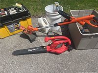 Homelite blower and Black & Decker trimmer with containers of garden chemicals and tools on pavement outdoors