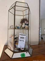 Front and side view of hexagonal glass and mirrored tabletop display cabinet showing porcelain doll and various figurines inside.