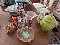 Overview of lot items on wooden table showing all items including covered dish, lidded ceramic pot, Murano-style candy bowl, bud vases, candleholders and horse cart figurine