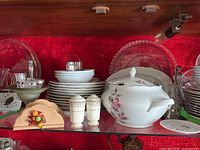 Shelf with white porcelain tureen, bowls, plates, glass plates, salt and pepper shakers, and napkin holder featuring painted fruit bouquet
