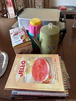 Photo showing assortment of small kitchen appliances including apple peeler box, insulated carafe, electric percolator, electric fry pan, and chafing dish