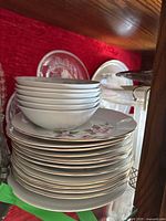 Photo of stacked ceramic plates and bowls with floral decoration and gold trim in wooden cabinet