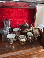 Bavarian and silver lustre espresso sets including pots, cream, sugar, cups, and saucers displayed on a shelf with red background.