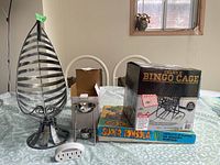 Photo of the lot on table showing metal fruit bowl, oil warmer box, Super Tombola box, and Deluxe Bingo Cage box.