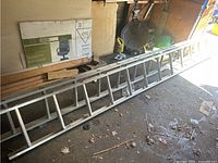 Two metal extension ladders, one longer and one shorter, lying on a garage floor next to cardboard boxes and various garage items.