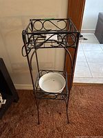 Side view of the black metal plant stand showing the geometric circle design with white ceramic dish on the removable lower shelf