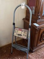 Front view of the Cosco two-step metal step ladder with packaging label attached on top and demonstration sticker on step