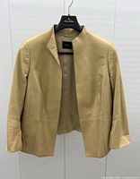 Front view of gold tone Akris leather jacket with slightly tailored seams and collarless neckline on a hanger.