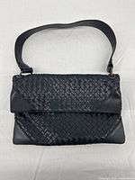 Front view of black woven leather handbag with shoulder strap and flap closure