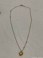 Full view of the delicate gold chain necklace with knots visible on the chain and heart-shaped pendant with pearl at the bottom.