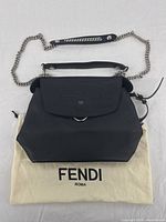Front view of black leather Fendi backpack with flap closure and chain-and-leather shoulder strap displayed on Fendi dust bag