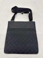 Full front view of bag showing black GG canvas body, leather flap and attached shoulder strap
