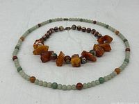 Both necklaces arranged side by side on white fabric background