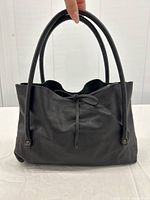 Front view of black leather handbag showing handles and drawstring tie closure