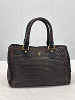 Front view of brown and black woven leather handbag on neutral background
