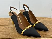 Angled front view showing black satin upper and gold leather trim on vamp