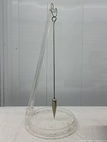 Full view of clear lucite sand tracing pendulum showing metal pendulum suspended from a lucite arm over a circular base containing white sand.