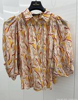 Front view of silk blouse on hanger showing the abstract female nudes pattern and puffed sleeves.