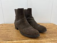 Pair of brown suede ankle boots shot at three-quarter angle on wooden surface