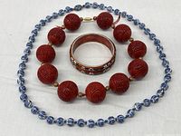 All three items displayed together: cinnabar bead necklace, porcelain bead necklace, enamel bangle