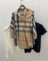 Three shirts hanging: beige check blouse at front, black polo and white button-down behind