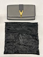 Front view of grey perforated leather clutch with Y clasp above dust bag.