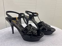 Perspective view of a pair of black patent leather platform stiletto T-strap sandals with ankle straps and gold-tone buckles