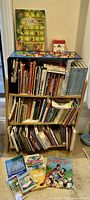Bookshelf filled with children's books, games, and puzzles arranged on shelves with some items on the floor in front