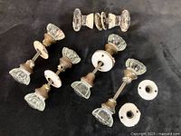 Photo showing all four pairs of antique clear glass doorknobs with attached spindles and two painted metal roses each, laid out on a black background.