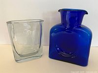 Two glass items: cobalt blue Blenko water bottle and clear glass vase with etched Viking ship.