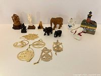 Photo showing an assortment of small figurines and ornaments including wood and resin gods, wooden elephants, porcelain lighthouse, hand-painted vase, and a crystal or glass piece