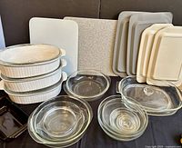 Full view of all items on display including white ribbed casseroles with lids, stacked clear glass bowls, amber bread loaf dish, two cutting boards, and various glass and silicone lids.