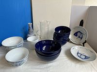 Full collection of assorted blue dishware including navy bowls, Chinese fish bowls, floral bowls, clear pitcher, white planter, and blue bud vase.