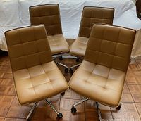 Set of four honey-caramel colored rolling side chairs with tufted vinyl upholstery and chrome legs.